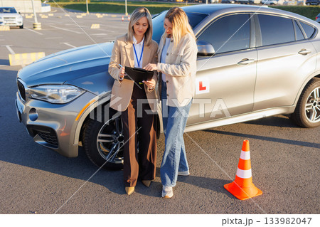 Driving instructor and student reviewing training results beside learner vehicle 133982047
