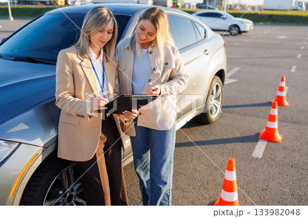 Driving Instructor Explaining Exam Checklist to Student Near Training Car Outdoors 133982048
