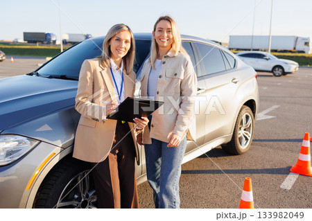 Driving Student and Instructor Reviewing Test Form Beside Training Vehicle 133982049