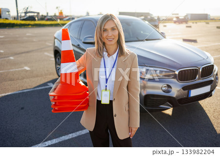 Driving instructor standing with traffic cones next to training vehicle at test site Driving instructor standing with traffic cones next to training vehicle at test site 133982204