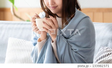 ブランケットを羽織って温かい飲み物を飲む女性 133982371