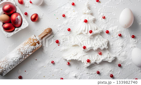white flour on the table in the shape of a christmas tree, red pearls scattered around it, a rolling pin and eggs next to a white background. 133982740
