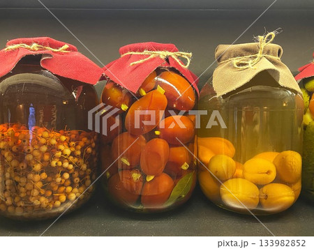 Homemade preserves in glass jars with fabric toppers and lids tied with twine. Pickled tomatoes, berries and apricots 133982852