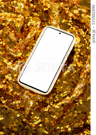 Smartphone with blank white screen on background of shiny golden fabric with sequins 133982890