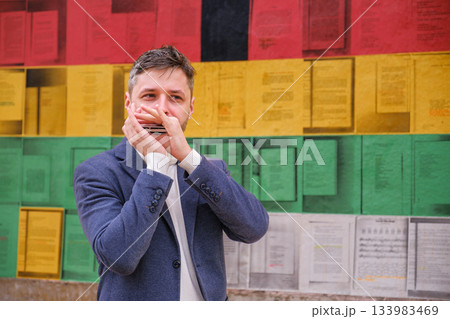 Man plays harmonica outdoors in city street Man plays harmonica outdoors in city street 133983469