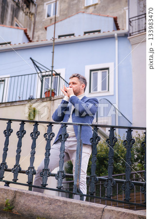 Man plays harmonica outdoors in city street 133983470