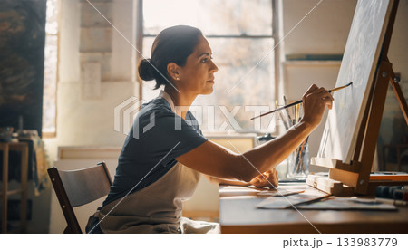 窓からの日差し：アトリエで集中してキャンバスに絵を描く女性 133983779