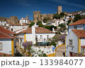 Obidos town featuring white houses, vibrant rooftops, and the impressive medieval castle under a blue sky. Portugal 133984077