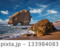 Penedo do Guincho rock at Praia da Santa Cruz as waves crash against the sandy shore during a colorful sunset. 133984083