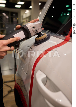 Polishing black car surface thoroughly, Detailed buffing to achieve showroom quality shine, Expert technician uses orbital buffer and foam pad to enhance vehicle gloss Polishing black car surface thoroughly, Detailed buffing to achieve showroom quality shine, Expert technician uses orbital buffer and foam pad to enhance vehicle gloss 133984101