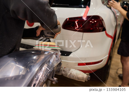 Hands refining car lamps professionally, Orbital buffer restoring clarity to headlights, Closeup of technician smoothing car headlight with orbital buffer and polishing tools Hands refining car lamps professionally, Orbital buffer restoring clarity to headlights, Closeup of technician smoothing car headlight with orbital buffer and polishing tools 133984105