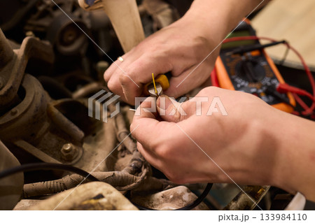 Electrical diagnostics performed on car wiring with multimeter tools, Technician connecting and repairing vehicle wiring under warm workshop lighting conditions Electrical diagnostics performed on car wiring with multimeter tools, Technician connecting and repairing vehicle wiring under warm workshop lighting conditions 133984110