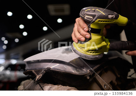 Hands refining car lamps professionally, Orbital buffer restoring clarity to headlights, Closeup of technician smoothing car headlight with orbital buffer and polishing tools Hands refining car lamps professionally, Orbital buffer restoring clarity to headlights, Closeup of technician smoothing car headlight with orbital buffer and polishing tools 133984136