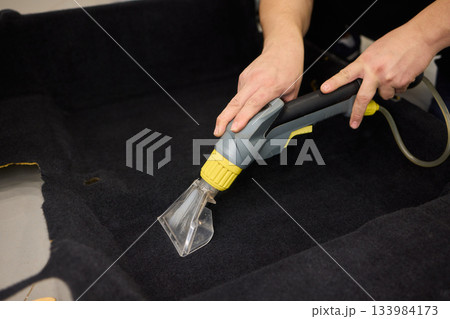 Automotive cleaning process, Professional vehicle upholstery maintenance and dirt removal, Detailed view of cleaning device removing grime from dark fabric upholstery 133984173