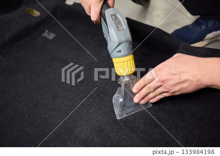 Automotive cleaning process, Professional vehicle upholstery maintenance and dirt removal, Detailed view of cleaning device removing grime from dark fabric upholstery 133984198