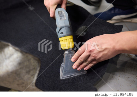 Automotive cleaning process, Professional vehicle upholstery maintenance and dirt removal, Detailed view of cleaning device removing grime from dark fabric upholstery 133984199