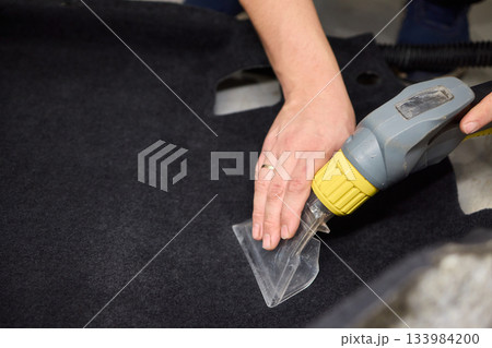 Automotive cleaning process, Professional vehicle upholstery maintenance and dirt removal, Detailed view of cleaning device removing grime from dark fabric upholstery 133984200