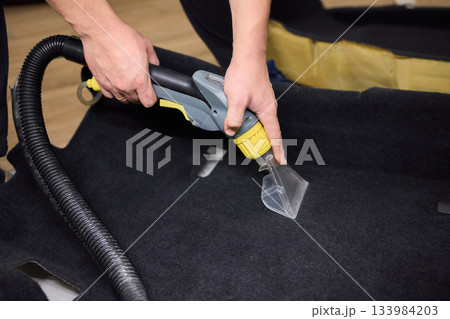 Automotive cleaning process, Professional vehicle upholstery maintenance and dirt removal, Detailed view of cleaning device removing grime from dark fabric upholstery 133984203