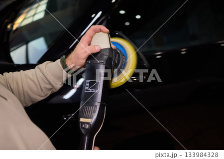 Polishing black car surface thoroughly, Detailed buffing to achieve showroom quality shine, Expert technician uses orbital buffer and foam pad to enhance vehicle gloss Polishing black car surface thoroughly, Detailed buffing to achieve showroom quality shine, Expert technician uses orbital buffer and foam pad to enhance vehicle gloss 133984328
