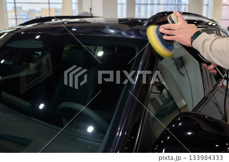 Polishing black car surface thoroughly, Detailed buffing to achieve showroom quality shine, Expert technician uses orbital buffer and foam pad to enhance vehicle gloss Polishing black car surface thoroughly, Detailed buffing to achieve showroom quality shine, Expert technician uses orbital buffer and foam pad to enhance vehicle gloss 133984333