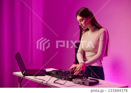 Female DJ mixing on turntables, colorful lighting studio, focused expression, hands adjusting mixer and laptop controls, wearing headphones, modern electronic music vibe, cinematic lighting Female DJ mixing on turntables, colorful lighting studio, focused expression, hands adjusting mixer and laptop controls, wearing headphones, modern electronic music vibe, cinematic lighting 133984376