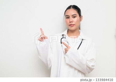 Woman Doctor with Stethoscope in White Uniform on Plain Background Pointing Finger Woman Doctor with Stethoscope in White Uniform on Plain Background Pointing Finger 133984410