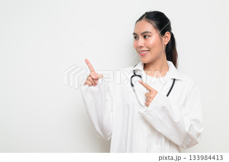 Woman Doctor with Stethoscope in White Uniform on Plain Background Pointing Finger Woman Doctor with Stethoscope in White Uniform on Plain Background Pointing Finger 133984413