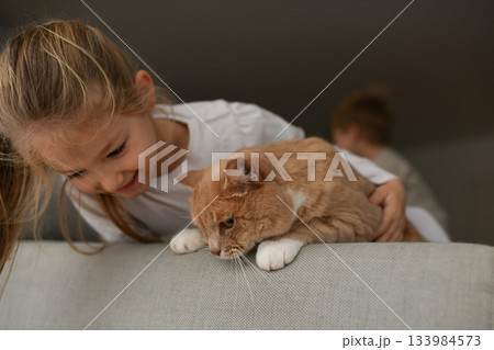 A girl near a ginger cat on the couch A girl near a ginger cat on the couch 133984573