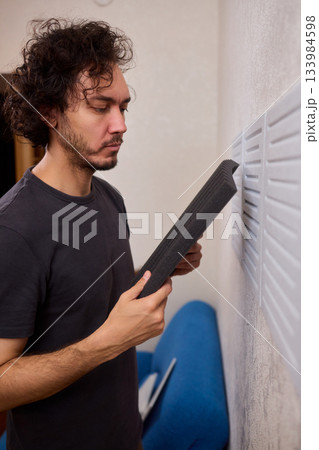 Closeup of foam insulation method, Hand pressing textured acoustic foam onto wall surface, Detailed shot of fingers securing black foam panels on gray wall Comparison of different foam rubber and Closeup of foam insulation method, Hand pressing textured acoustic foam onto wall surface, Detailed shot of fingers securing black foam panels on gray wall Comparison of different foam rubber and 133984598
