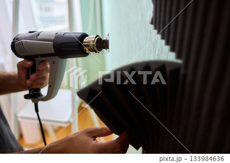Craftsman carefully detaching acoustic panels indoors, Individual skillfully peels acoustic insulation from wall using heat and precise hand movements for studio setup 133984636