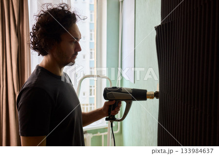 Craftsman carefully detaching acoustic panels indoors, Individual skillfully peels acoustic insulation from wall using heat and precise hand movements for studio setup Craftsman carefully detaching acoustic panels indoors, Individual skillfully peels acoustic insulation from wall using heat and precise hand movements for studio setup 133984637