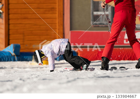 The girl fell while learning to ski.Ski coach giving a lesson to a child 133984667