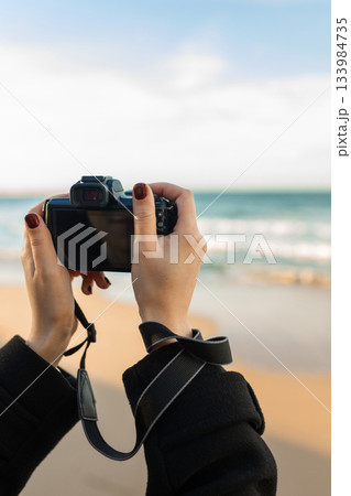 Close-up of woman holding a professional camera on the beach during golden hour, focusing on the lens and capturing outdoor photography moments. 133984735
