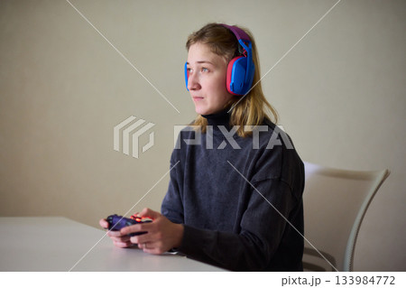Casual female gamer with cerebral palsy, Relaxed woman with gaming controller, Young woman plays video game comfortably at home, Female gamer intently engaging with console in cozy living space 133984772