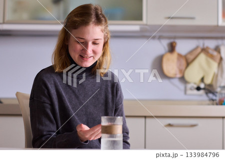 Self reliant woman handles morning pills in peaceful kitchen setting, Woman with cerebral palsy diligently manages her daily medication routine independently at home Self reliant woman handles morning pills in peaceful kitchen setting, Woman with cerebral palsy diligently manages her daily medication routine independently at home 133984796