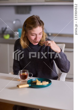 cerebral palsy Young woman smiling with tea and cheesecake, Casual domestic setting featuring woman indulging and relaxing, Relaxed young woman savoring cake and tea at sunlit kitchen table 133984812