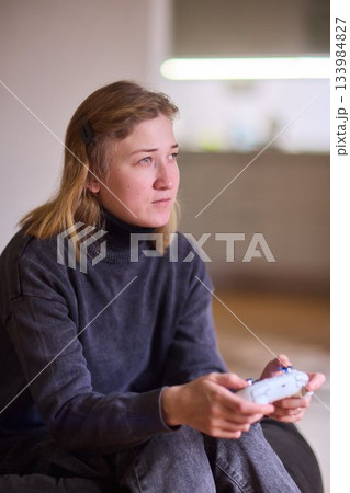 Casual female gamer with cerebral palsy, Relaxed woman with gaming controller, Young woman plays video game comfortably at home, Female gamer intently engaging with console in cozy living space 133984827