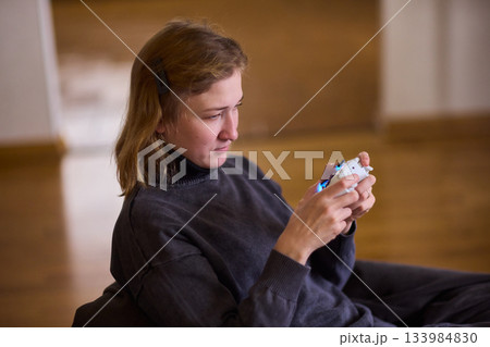 Casual female gamer with cerebral palsy, Relaxed woman with gaming controller, Young woman plays video game comfortably at home, Female gamer intently engaging with console in cozy living space 133984830