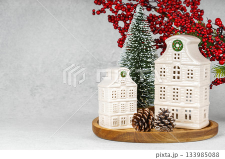 Ceramic Christmas houses with pine Tree and winter decorations on wooden tray on white background 133985088
