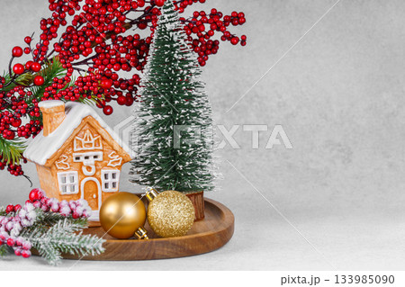 Gingerbread style ceramic Christmas house with ornaments, holly berries and snowy spruce tree Gingerbread style ceramic Christmas house with ornaments, holly berries and snowy spruce tree 133985090