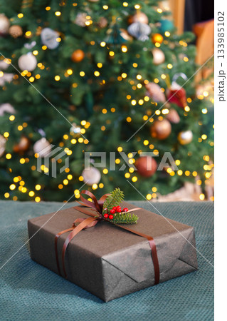 Christmas gift box decorated with ribbon and red berries in front of glowing festive tree lights 133985102