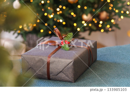 Christmas gift box decorated with ribbon and red berries in front of glowing festive tree lights 133985103