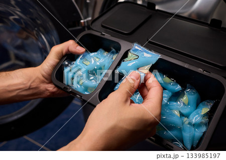 Laundry pod placement, Load blue detergent capsules into machine for hygienic washing, Preparing laundry by placing capsules carefully into washing machine for cleanliness Laundry pod placement, Load blue detergent capsules into machine for hygienic washing, Preparing laundry by placing capsules carefully into washing machine for cleanliness 133985197