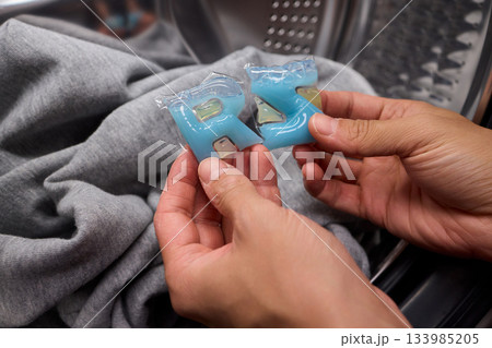 Inspecting laundry pod on sweater, Closeup of hands testing cleaning tablet, Detailed view of hand assessing laundry pod for quality and proper dissolution process Inspecting laundry pod on sweater, Closeup of hands testing cleaning tablet, Detailed view of hand assessing laundry pod for quality and proper dissolution process 133985205