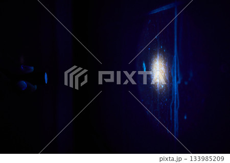 Surface analysis under ultraviolet reveals hidden contaminants, Facility inspector uses UV illumination to identify unseen dirt and contamination on tiles in darkroom 133985209