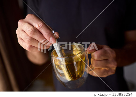 Warm tea preparation, Relaxed moment with steaming hot beverage in tranquility, Quiet domestic setting emphasizing mindful hand movements during tea stirring activities 133985254