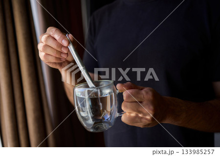 Warm tea preparation, Relaxed moment with steaming hot beverage in tranquility, Quiet domestic setting emphasizing mindful hand movements during tea stirring activities 133985257