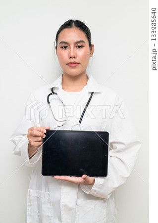 Asian Woman Doctor in White Uniform Using Digital Tablet Computer on Plain White Background 133985640