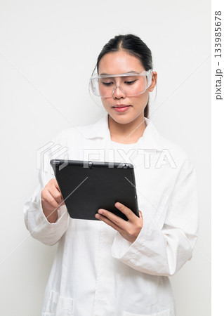 Young Female Scientist in Protective Goggles and Lab Coat on White Background Using Tablet Computer 133985678