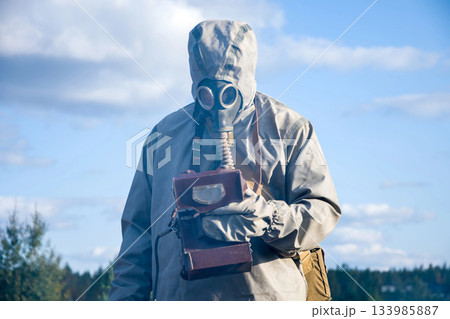 Military dosimetrist measures radiation on a grassy area. chemical protective SUIT and gas MASK, Sunny day 133985887